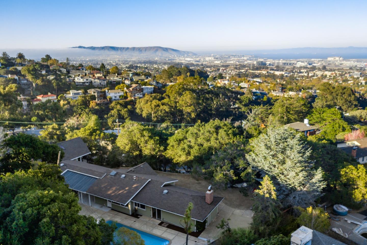 Tucked in the treetops above Millbrae Ave with airport/bay/east bay views thru the trees. Large calm home with lots of space & great natural light on a tree-lined half+ acre lot with a large level area, pool, an in-law unit, & a large detached workshop of ~600 sf. Need space for multi-generations, a home office, & a large workshop for a home-based business? This home would be ideal.  Convenient one-level living: formal entry, bright & spacious kitchen for multiple cooks, open floor plan, dining with floor-to-ceiling windows, home office with beautiful french doors, an enormous living area for large gatherings that can overflow outside. Primary suite opens onto the pool area, dual bedrooms w/ power skylights with black-out shades. Beautiful in-law unit in the trees with private access, kitchen, dining, living, bath & laundry room. Two car garage, storage room & huge workshop.  This is a flexible-use property that will serve many needs. 2 full kitchens, 2 laundry rooms- lots of options.